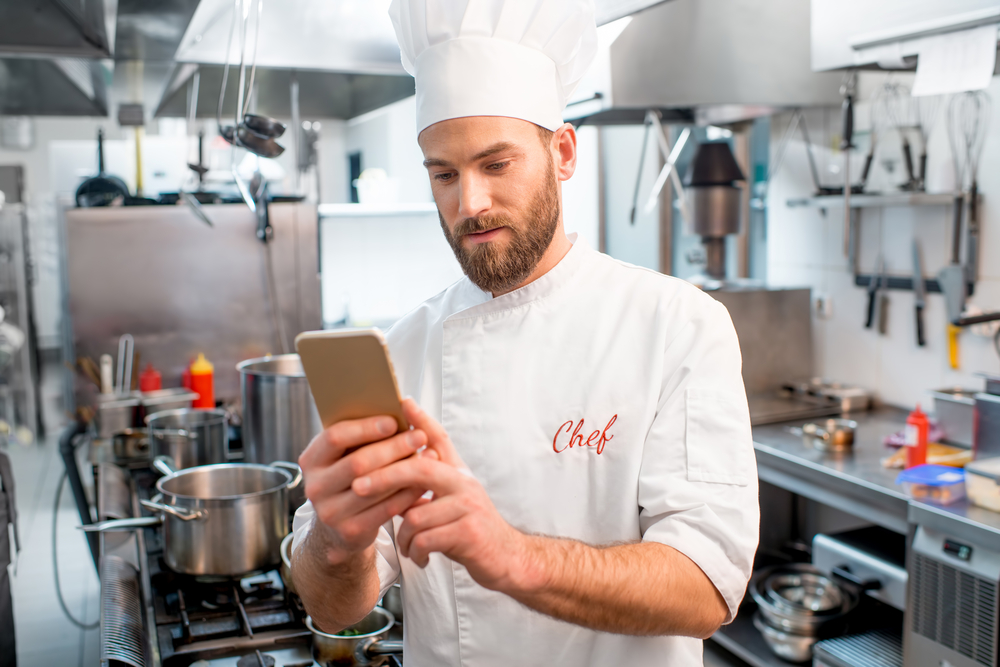 Chef,Cook,Using,Smart,Phone,At,The,Restaurant,Kitchen