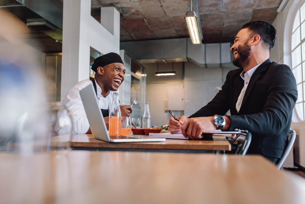 Smiling,Restaurant,Manager,Sitting,At,Table,And,Talking,With,Chef.